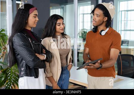 Diverse coworkers collaborating on project in modern office meeting area with tablet and headphones Stock Photo