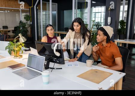 Diverse coworkers analyzing data on desktop monitor with printed charts at coworking office Stock Photo