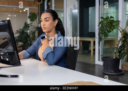 Woman wearing denim shirt sitting at white desk in open-plan office using desktop computer monitor Stock Photo
