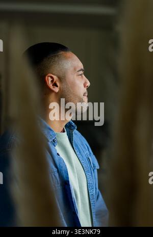 Hispanic man standing in living room amid dried pampas grass, wearing denim shirt and sweater Stock Photo