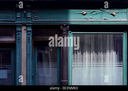 Close-up of an ornate, weathered green door and window frame with curtains Stock Photo
