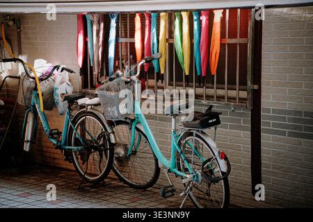 Taipei, Taiwan - May 16, 2023: Colorful umbrellas hung on iron bars beside teal bicycles with baskets parked along a brick wall. Stock Photo