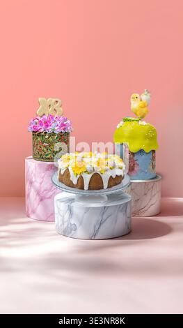 Stylish studio composition of three beautifully decorated Easter kulichi on marble pedestals against a soft pink background. Stock Photo