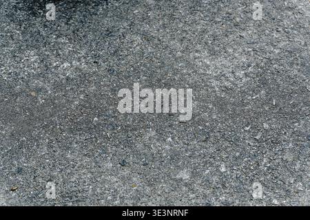 Top-down close-up of gray asphalt pavement showing granular stone texture and subtle cracks, ideal as a seamless urban background or design overlay. Stock Photo