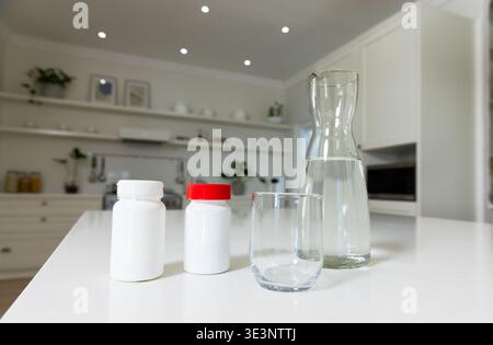 White glossy island holding two pill bottles with red cap, glass carafe with water in kitchen Stock Photo