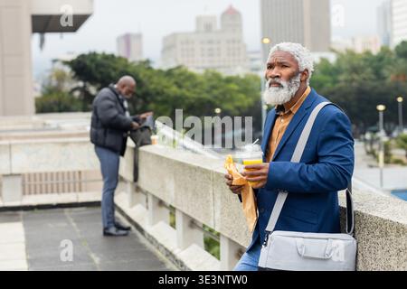 African american colleagues standing on balcony sharing pastry and coffee during break Stock Photo