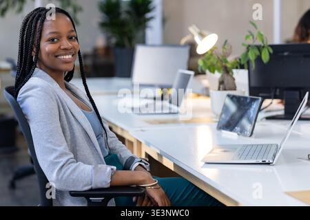 African American woman typing on laptop sitting in chair at office desk wearing blazer, copy space Stock Photo