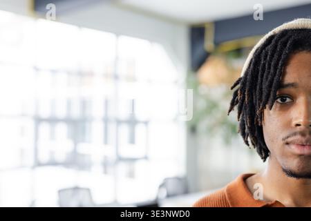 African American man wearing orange sweater standing in modern office by grid windows, copy space Stock Photo