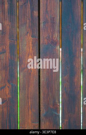Close up of dark stained wooden boards with visible grain and narrow gaps showing soft green background. Stock Photo