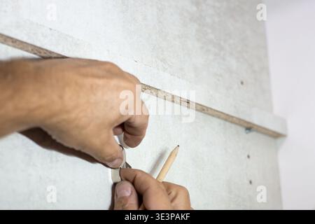 Worker's hands marking a wall with a pencil using a wooden guide Stock Photo