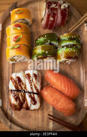 Assorted sushi rolls and nigiri arranged on wooden platter showcasing traditional Asian cuisine, including salmon nigiri, eel nigiri, and colorful maki rolls with garnishes Stock Photo