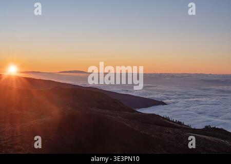 Sunrise above clouds in Teide National Park Tenerife Spain with sun rays over volcanic mountain ridge scenic landscape Stock Photo