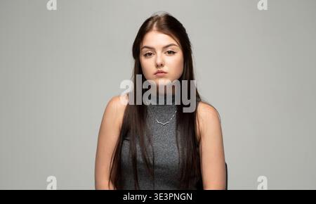 Young brunette woman looking at the camera with a serious and neutral expression, posing in a studio Stock Photo