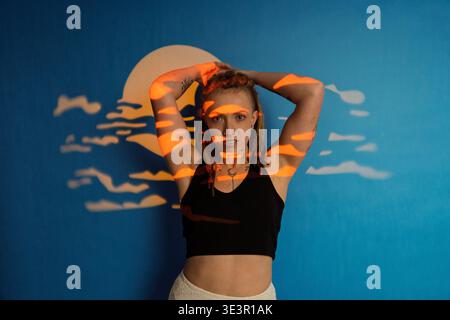 Woman with dreadlocks looking at camera, illuminated by abstract light shapes over a blue background Stock Photo