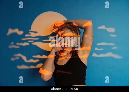 Woman with dreadlocks posing, illuminated by orange sunset projection on a blue artistic backdrop Stock Photo