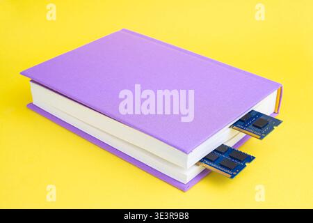 A purple book sits on a bright yellow surface, with computer chips sticking out from its spine, combining ideas of tech and reading. Stock Photo