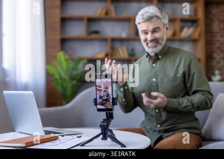 Mature man presenting and recording an educational video with his smartphone on a tripod, providing online coaching or participating in a webinar from his home office Stock Photo