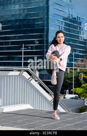 Woman performing leg stretch on tiled pedestrian ramp by metal railing, copy space Stock Photo