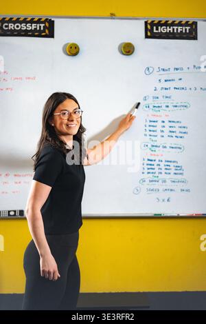 Female coach teaching crossfit workout on whiteboard in gym Stock Photo