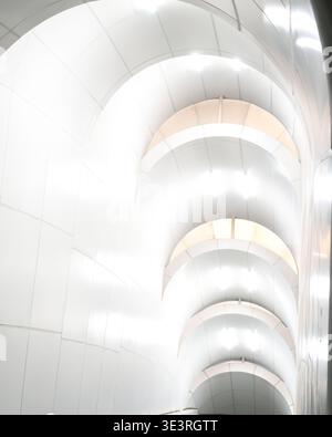 An abstract interior view of a brightly illuminated modern corridor featuring a repeating series of smooth white curved archways and recessed lighting Stock Photo