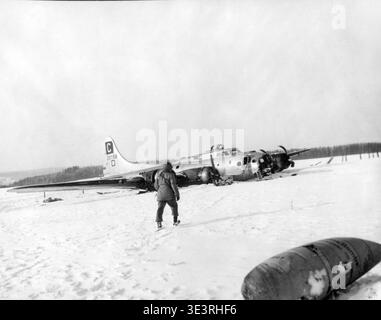 A crashed B-17 Flying Fortress bomber lies in a snowy field near Remagne, Belgium, during the Battle of the Ardennes on January 13, 1945. A soldier approaches the wreckage in this historical black and white photograph. Stock Photo