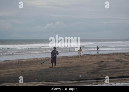 Man Holding a Rake on a Littered Shoreline Stock Photo
