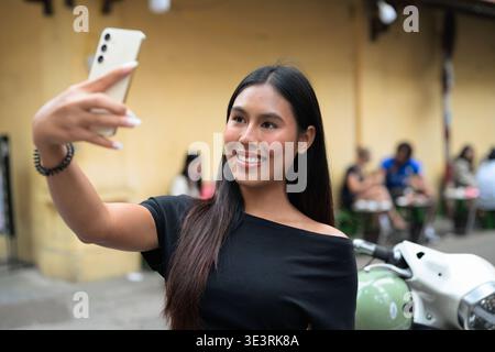 Young Thai Woman Taking Selfie with Mobile Phone Outdoors in Hanoi Stock Photo