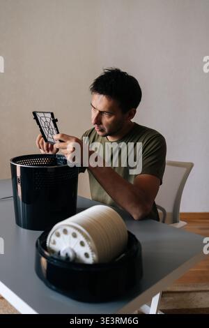Vertical portrait of focused man holding inspecting air humidifier filter, performing maintenance and cleaning to ensure clean, healthy air in home Stock Photo