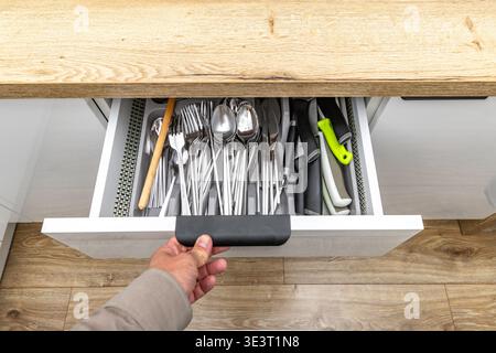 Open cutlery drawer, knives, forks, spoons, teaspoons, tableware placed in the drawer, new practical kitchen furniture with white drawers, wooden furn Stock Photo
