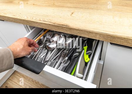 Open cutlery drawer, knives, forks, spoons, teaspoons, tableware placed in the drawer, new practical kitchen furniture with white drawers, wooden furn Stock Photo