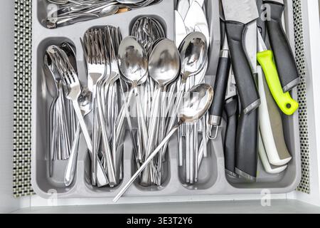 Open cutlery drawer, knives, forks, spoons, teaspoons, tableware placed in the drawer, new practical kitchen furniture with white drawers, wooden furn Stock Photo