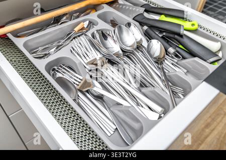 Open cutlery drawer, knives, forks, spoons, teaspoons, tableware placed in the drawer, new practical kitchen furniture with white drawers, wooden furn Stock Photo