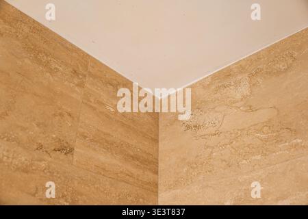 Detailed shot of a room corner featuring high quality travertine tiles with natural textures and patterns, joined seamlessly with a smooth white ceili Stock Photo