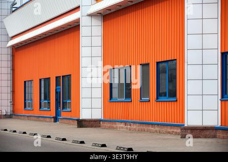 Architectural facade with orange white and blue cladding corrugated metal panels, glass windows of industrial or commercial building, contemporary arc Stock Photo
