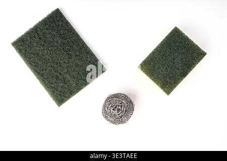 Flat lay of three common household dishwashing and cleaning tools on a white surface. Includes a large green nylon abrasive pad, a green and yellow du Stock Photo