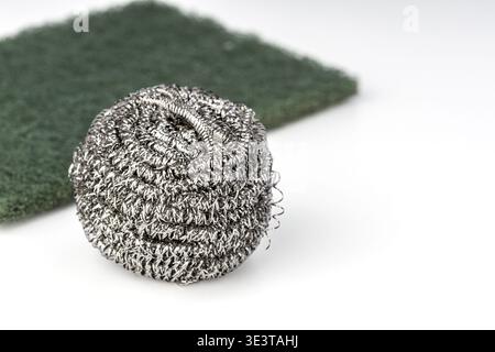 A detailed close-up of a stainless steel wool scrubber ball with interwoven metallic wire loops, placed beside a green abrasive nylon scouring pad on Stock Photo