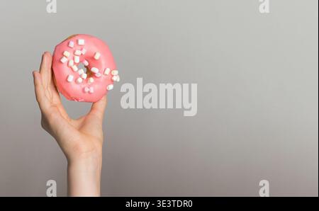 Pink Donut with white marshmallows in human hand, sweet dessert food Stock Photo