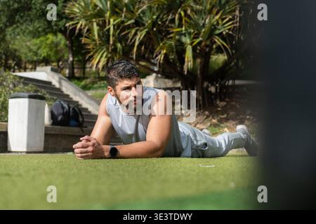 Young athletic man lying on green grass after exercising outdoors, relaxing and recovering after a workout in a park. Healthy lifestyle, fitness, fati Stock Photo