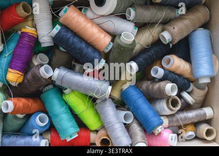 Various spools of multicolored sewing thread filling a box, creating a textile background for craft and fashion concepts Stock Photo