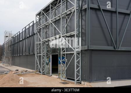 Modern industrial warehouse under construction featuring steel frame structure, dark metal facade and glass entrance at building site Stock Photo