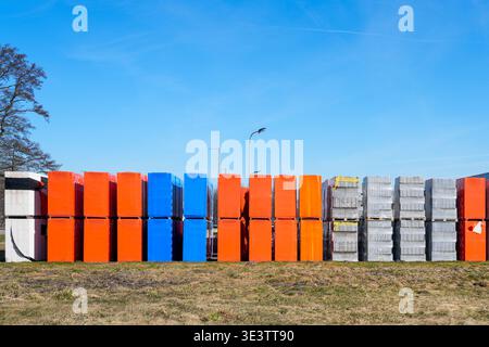 Bright orange, blue and gray construction materials stacked in rows on pallets outdoors, forming a geometric pattern under clear sky Stock Photo
