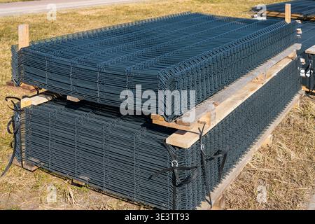 Bundles of steel wire mesh fence panels stacked on wooden pallets outdoors, used for reinforcement in construction and infrastructure projects Stock Photo