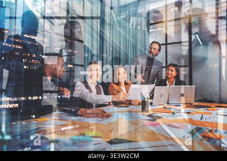 Group of people having a meeting in an office setting at night discussing ideas and reviewing documents and reports Stock Photo