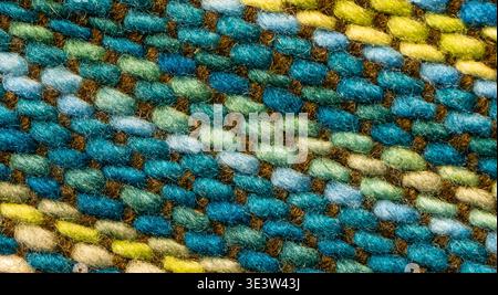 Close-up of a woven textile fabric showing blue, green and yellow threads. The detailed pattern highlights the texture and craftsmanship of handmade m Stock Photo