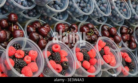 Assorted fresh berries including raspberries, blackberries, cherries and blueberries arranged in plastic cups at a market. The colorful composition hi Stock Photo