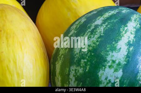 Close up of whole watermelon and yellow melons displayed at a market stall, showing natural rind texture and color contrast, suitable for fresh produc Stock Photo