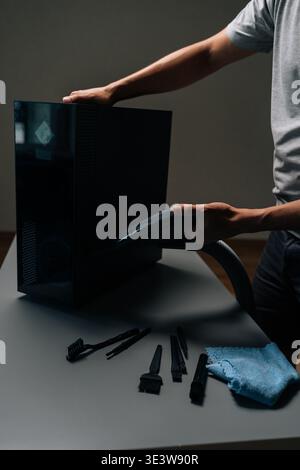Vertical cropped shot of computer technician cleaning computer case with vacuum cleaner, different brushes and microfiber cloth on table, performing Stock Photo