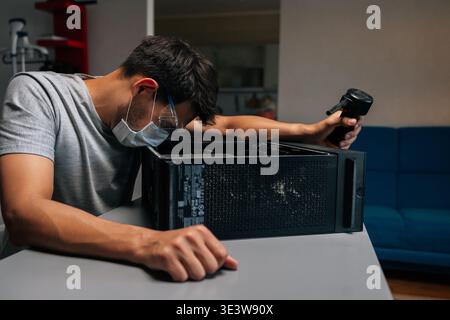 Side view of technician in face mask and safety glasses cleaning computer case using small vacuum cleaner, demonstrating proper maintenance procedures Stock Photo