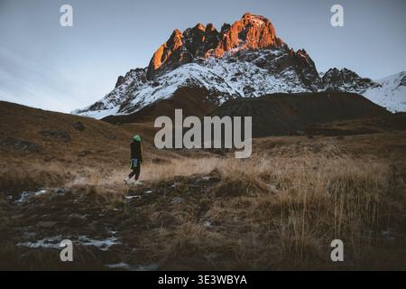 Female hiker hike trekking in beautiful Juta valley hiking route with scenic mountain snowy peak background. Kazbegi national park landscape Stock Photo