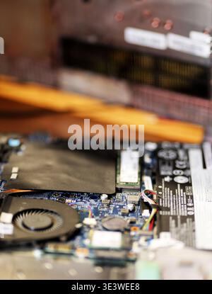 An opened laptop placed on a wooden surface reveals internal components including cooling fan, copper heat pipe, motherboard, RAM slots Stock Photo